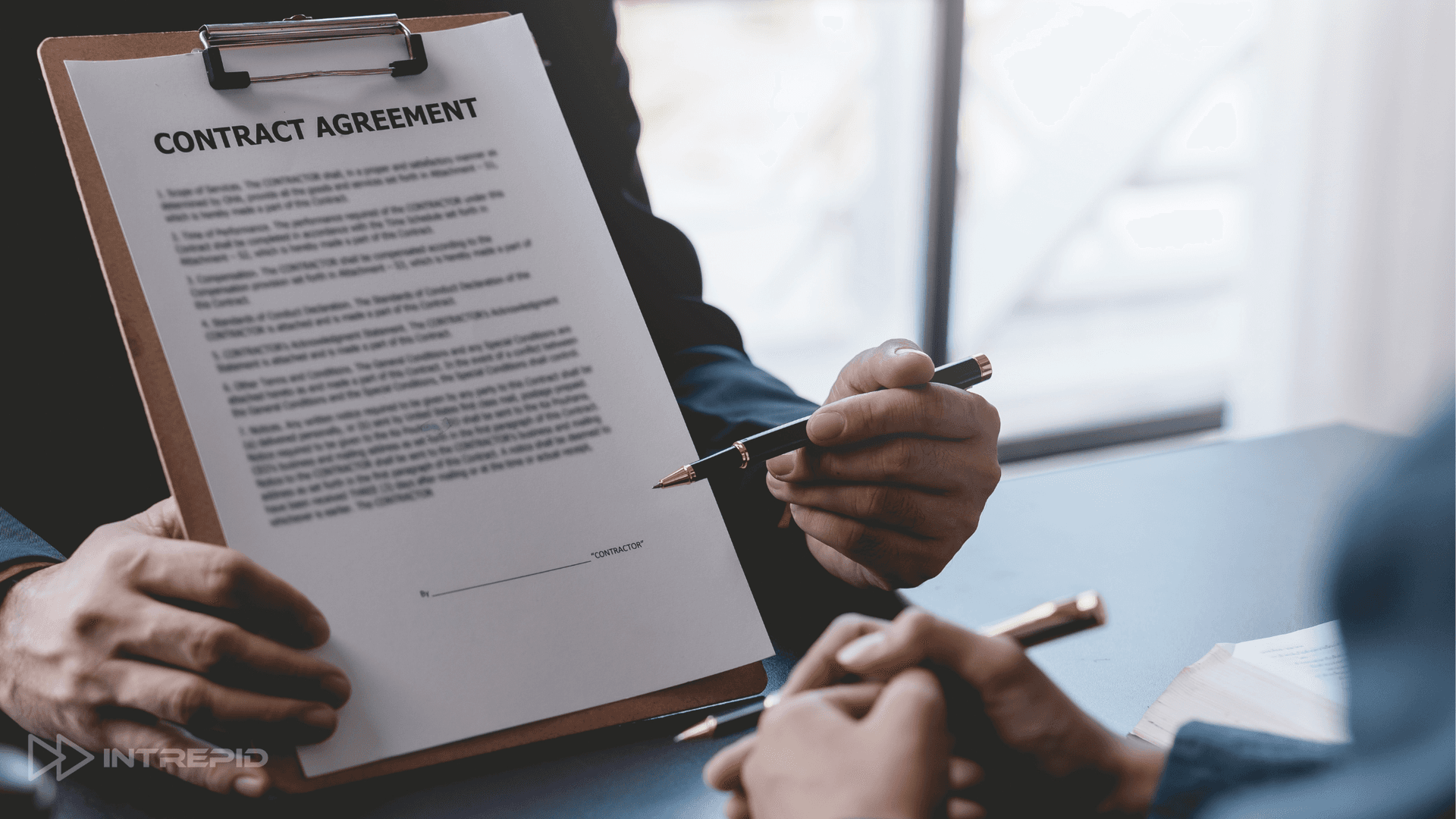 two men in suits holding pens, one man showing the other a contract on a clip board