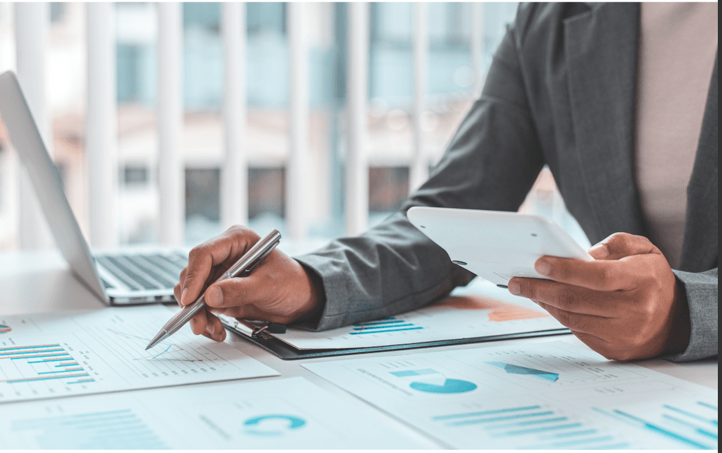 business person with a calculator in hand looking at charts next to an open lap top