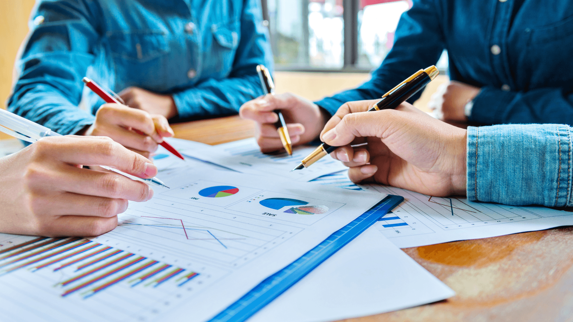 several hands working over multiple reports and charts spread out over conference table