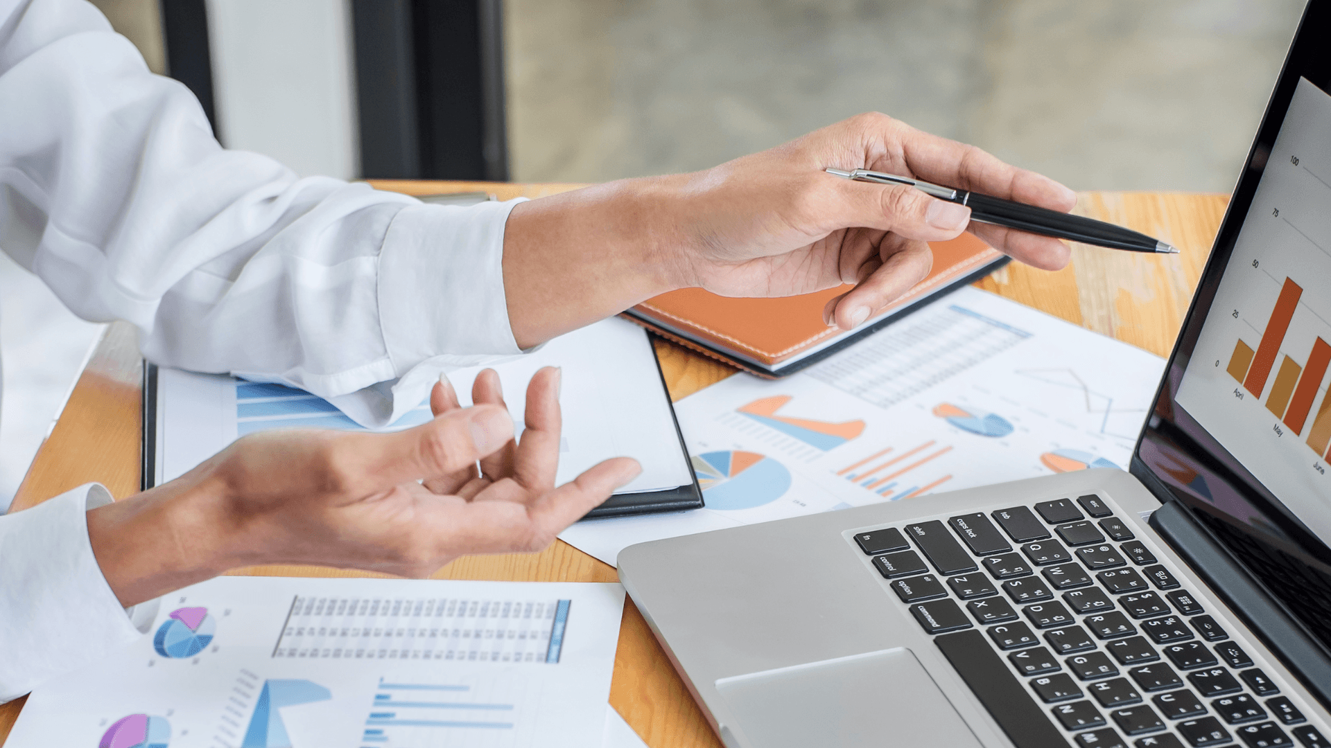 business persons hands, printed reports, laptop displaying graphs