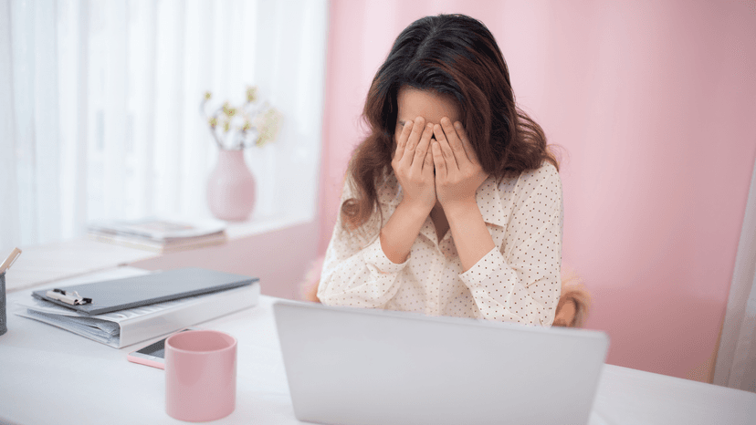 woman sitting at desk with hands over her face in despair