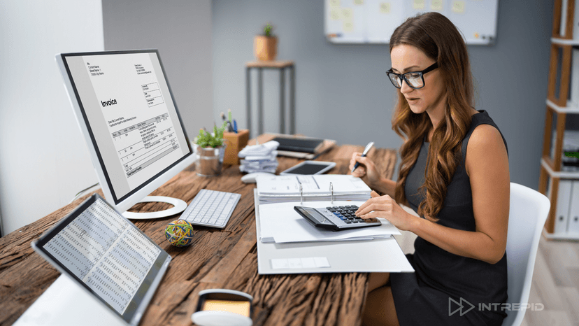 Businesswoman managing invoices and financials on screen and paper, representing flexible AR-backed funding solutions like Intrepid Finance's FlexAR.